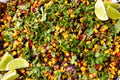 Colorful salad with corn, black beans, and cilantro garnished with lime wedges.