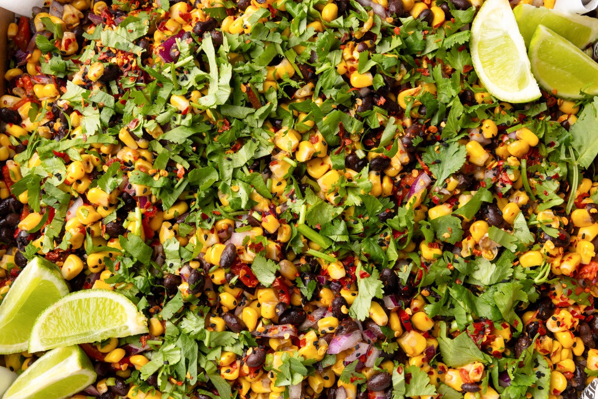 Colorful salad with corn, black beans, and cilantro garnished with lime wedges.