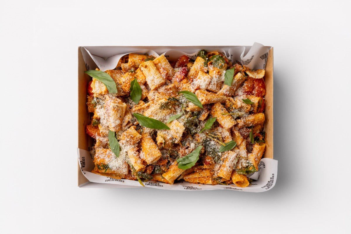 Box of pasta with greens and cheese on a white background